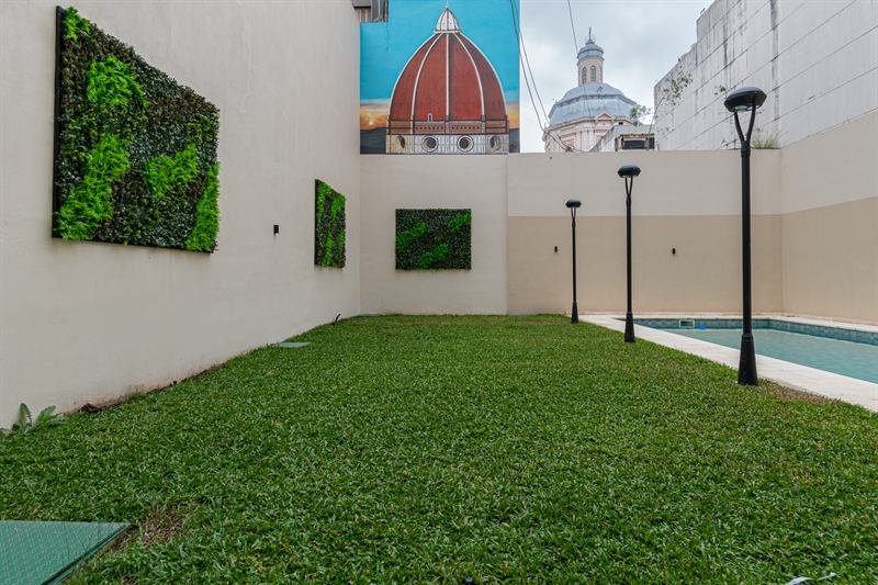 Patio con jardín vertical, césped y piscina, con cúpulas históricas de fondo